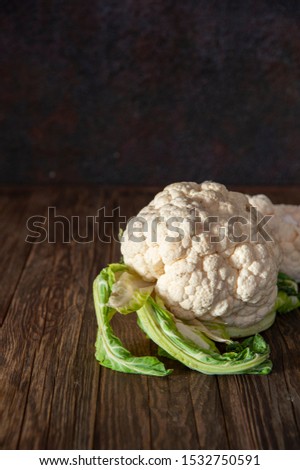 Autumn harvest. On a table of rough wood lies a fresh velvet of cauliflower, lit by the sun. In the background is the rough metal surface of the wall.