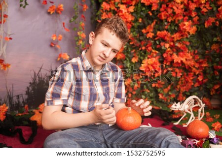 Photo of angry young man on halloween wearing classical plaid shirt holding orange pumpkin over street background with autumn leaves