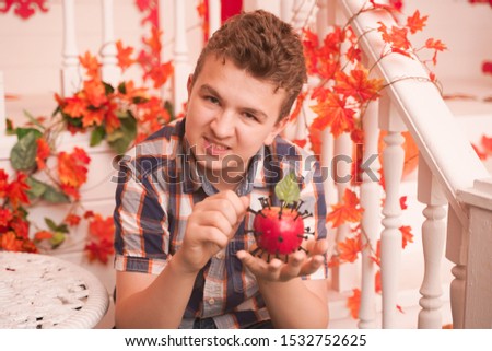 angry boy sits on the porch of his house decorated for Halloween. he is holding a toy Apple pierced with sharp iron screws. a young man tries to use voodoo magic.