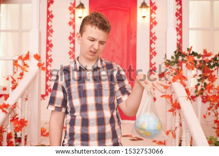 horizontal photo of an emotional teenager holding a planet in a bag and thinking about how his generation will live. concept of planet earth suffering and suffocating from plastic and overheating.