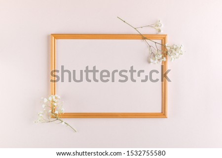 Greeting card concept. Sprigs of white flowers and a wooden frame on a beige pastel background. Top view composition with copy space