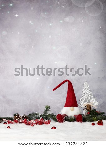 a little imp sit in a pine branch decoration with a christmas tree in the back and some gift boxes red berries and pineapples around him for the christmas mood on a grey sky background