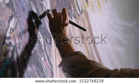 Artist designer draws an eagle on the wall. Craftsman decorator paints a picture with acrylic oil color brush. Close-up dark magic cinematic look. Painter dressed in a paint coat. Indoor.