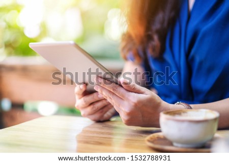 Closeup image of a woman holding and using tablet pc with coffee cup on the table