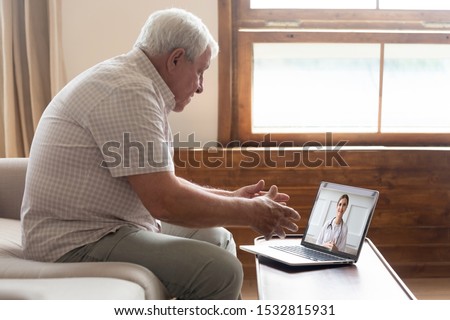 Elderly 70s man seated on sofa make distant video call, senior patient look at laptop screen communicating with doctor therapist online, older generation and modern tech application easy usage concept Royalty-Free Stock Photo #1532815931
