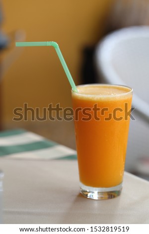 Glass of refreshing orange juice with a green drinking straw. Delicious, healthy and full of vitamin c. Still life photo with neutral colored soft background. Closeup color image.