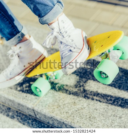 Close up of sport woman's legs in jeans and white sneakers extremely ride penny board skateboard. Modern urban hipster girl have fun. Good sunny summer day for lifestyle skateboarding and have fun.