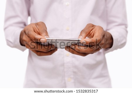 Unrecognizable man holding smartphone in horizontal orientation playing video games over white background, closeup