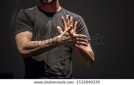 Sign language man interpreter gestures over stage during public event. Zenithal spot lighting his hands