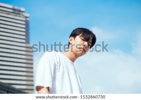 Herizontal low angle portrait picture of cute guy with high building and clear sky as a background.