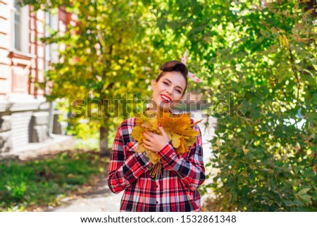 Beautiful woman with make up and hair in pin up holding big bouquet of maple yellow leaves in a sunny autumn day.