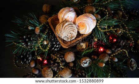 Christmas decor - meringues on a dish among green pine branches,  nuts, cones and red balls