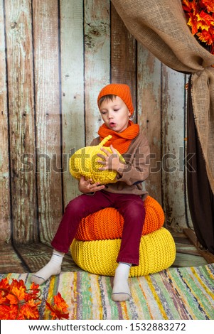a boy in an orange scarf and hat sits on a background of wooden scenery