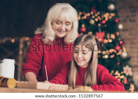 Portrait of nice attractive kind dreamy cheerful cheery granny pre-teen grandchild writing letter to Santa eve noel December time at decorated industrial brick wood loft style lights interior house