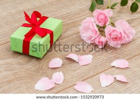 Gift box with red ribbon, rose petals and beautiful pink roses on the wooden background. Concept of giving a gift on holidays. Top view.