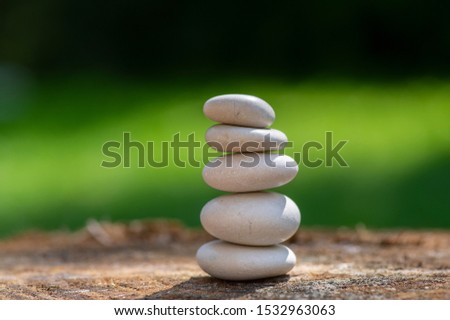 White five stones cairn in daylight, poise light pebbles on wooden stump in front of green natural background, zen like sculpture, simplicity, harmony and balance