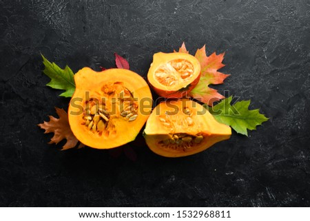 Autumn vegetables. Pumpkin with pumpkin seeds and autumn leaves. flat lay. On a black stone background. Top view. Free space for your text.