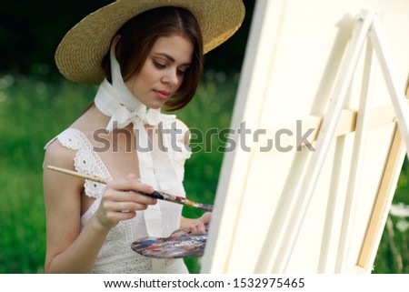 young woman in a hat paints a picture in nature
