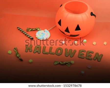 Halloween orange pumpkin bucket with sweet candy snack and alphabet biscuits “HALLOWEEN” on orange background, Halloween decoration concept.