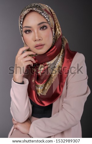 Fashionable female model wearing black inner and pink blazer with colorful hijab isolated on grey background. Stylish Muslim hijab fashion lifestyle portraiture concept.