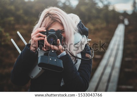 Focused blonde girl is making a photo with her photo camera while walking in the park.