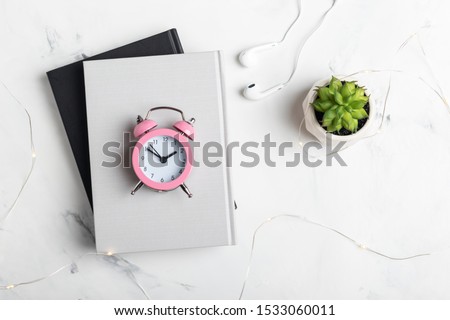 Small pink alarm clock on a stack of books on a white marble background. Working space