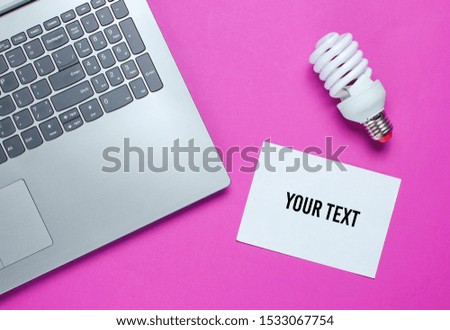 Modern laptop, spiral light bulb and sheet of white paper for copy space on pink background. Idea concept. Top view