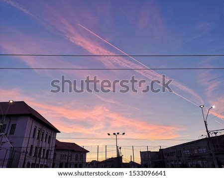 Photo of a beautiful blue sky decorated with orange and purple clouds at sunset, seen through small city buildings and electricity cables.