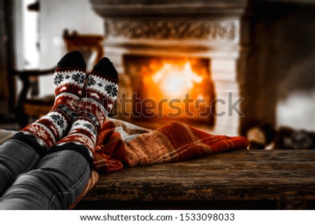 Woman legs with christmas sock on table and blurred home interior with fireplace. Free space for your decoration and dark mood photo style. 