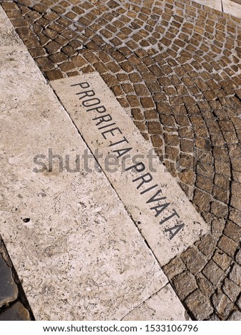 Marble plaque on asphalt and geometric pavement with the words PRIVATE PROPERTY in Italian seen from above