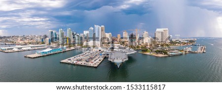 Amazing panoramic view of the San Diego downtown by the harbour with many skyscrapers and huge aircraft carrier docked by the pier.