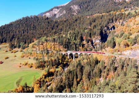 A local train of Rhaetian Railway (Rhatische Bahn) traveling across Schmittentobel Viaduct on a brisk autumn day, with beautiful fall colors on the mountainside, in Filisur, Grisons, Switzerland
