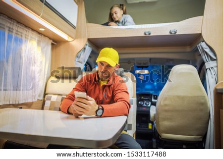 Family Spending Time Inside Camper Van RV Motorhome with Their Smartphones. Internet Connection While RVing Concept Photo. Campsite WiFi Signal.