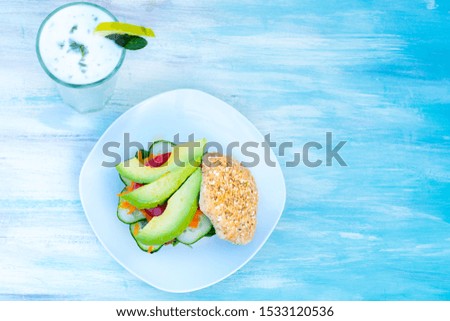 Cenital picture of a vegan sandwich on wholemeal bread, pickles and avocado, with a lemonade, on a light blue background