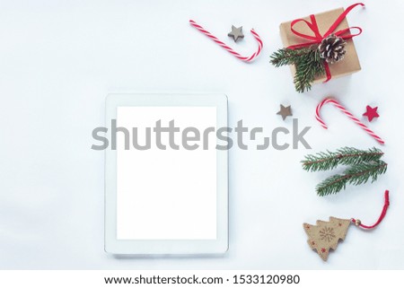 Christmas layout with tablet computer with blank screen, gift in a box, fir twigs,  red candy canes on white background, top view, flat lay, copy space