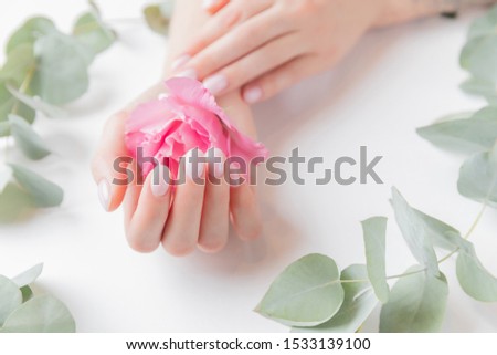 Stylish plain female hand manicure gel polish on white background with flower, top view. Concept natural organic skin care.