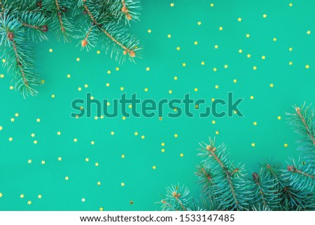 Christmas composition with borders of fluffy green fir branches and golden confetti stars sparse on trendy mint background. Top view, lat lay style, copy space for text.