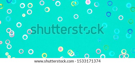 Colorful holographic foil confetti banner background. Pastel colored pink, blue and yellow circles sparse on trendy mint colored paper. Simple holiday concept. Top view, flat lay, copy space.