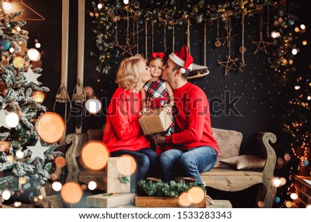Christmas family with baby smiling and kissing near the Xmas tree. Living room decorated by Christmas tree and present gift box, the light give cozy atmosphere. New Year theme