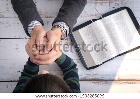 Top view closeup of a father and his little son's hands praying together after bible study in the morning. Christianity, Parenting and Raising child in God's way, Thankful moment, Happy father's day. Royalty-Free Stock Photo #1533285095