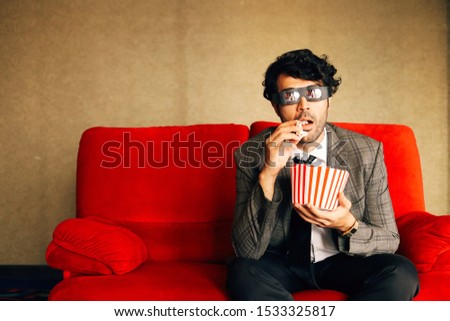 A Happy man sitting on red sofa and wearing 3D glasses,He’s watching movie at home.