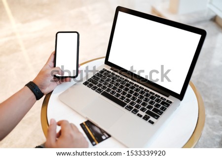 Close up of man using blank cell phone,laptop and credit card sending massages shopping online or reporting lost card, fraudulent transaction within the coffee shop