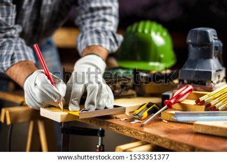 Adult carpenter craftsman wears protective leather gloves, with a pencil and the carpenter's square trace the cutting line on a wooden table. Construction industry, housework do it yourself.