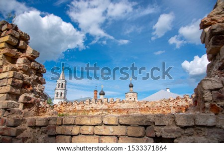 In the doorway of a ruined monastery wall visible to the monastic buildings on the background of blue cloudy sky.The picture looks like a postcard.