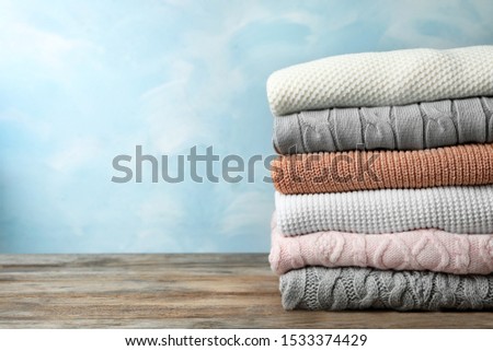 Stack of warm clothes on wooden table against light blue background, space for text. Autumn season