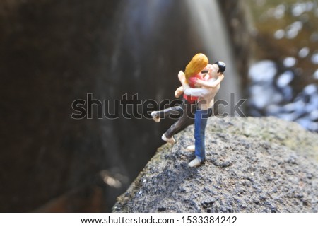 Miniature couple hugging in the rock mountain and blurry waterfall background, valentine concept 