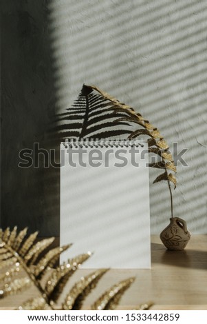 Modern trend home decor mock-up with shadows. Fall autumn minimal mock up with open empty note pad, golden dry leaves and candle on grey concrete wall background.