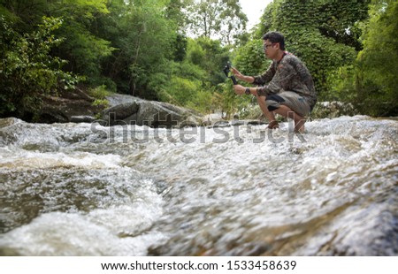 Traveller holding stabilizer for smartphone while taking photo in waterfall.