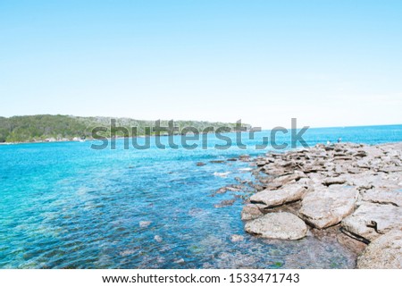 Amazing turquoise blue ocean landscape with rock formations at Near Bare Island, La parouse Sydney. Sunny day seascape with water reflection and commercial industry in the background