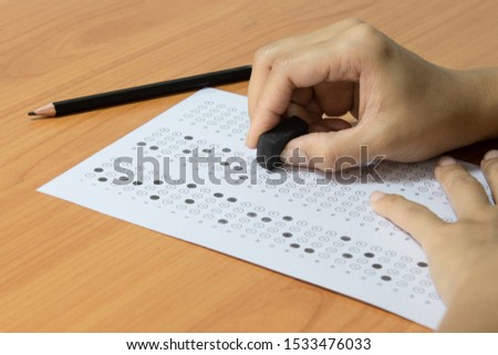 selective focus of right hand erasing an answer on a test answer sheet with a black rubber